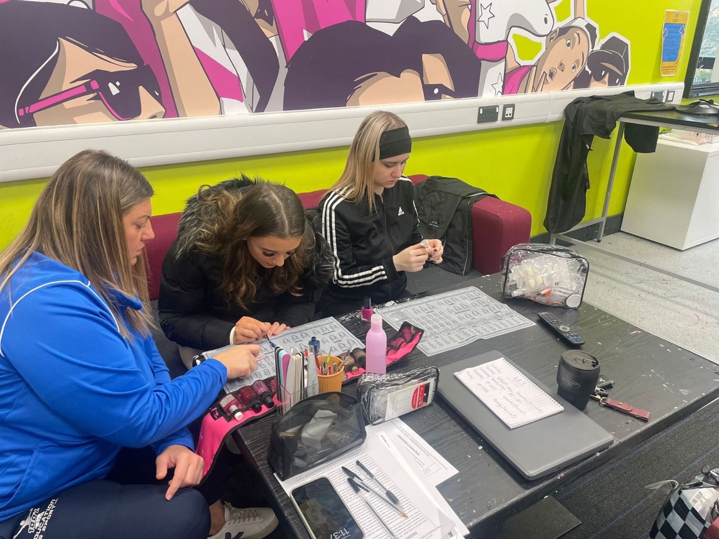 A mentor in blue kit guiding students through a practical beauty training session