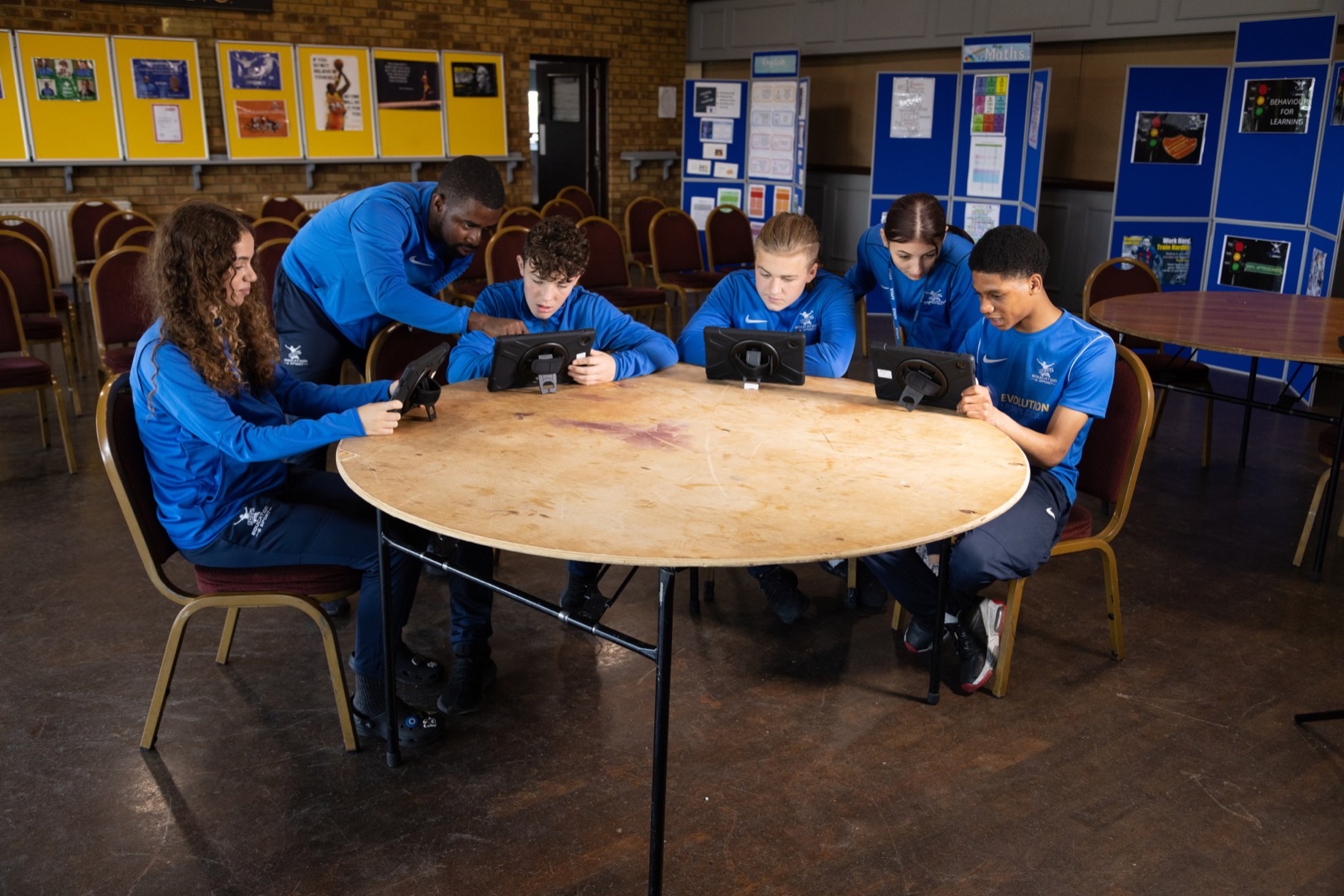 Students in blue Evolution kit working on tablets with a mentor guiding the group