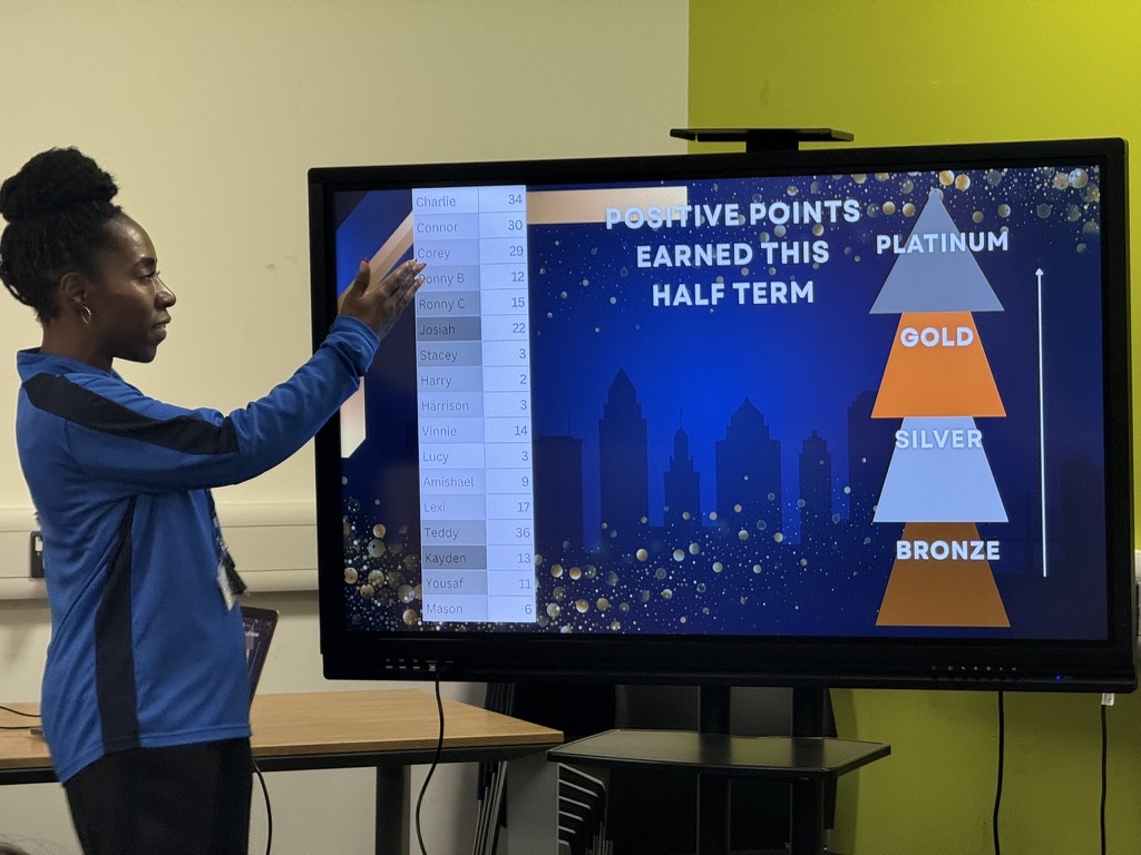 A staff member celebrating student progress on the half-term positive points board