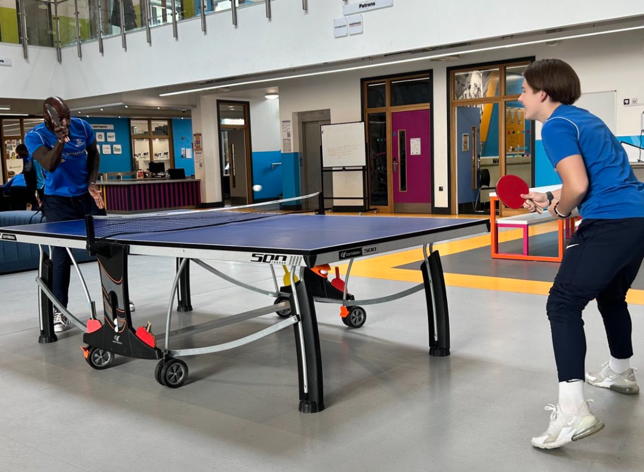 A mentor and student playing table tennis in a bright indoor centre