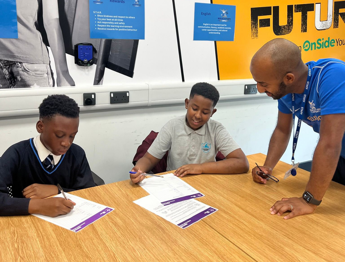 A member of staff mentoring young people as they work at a table