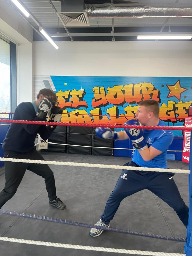 Two students sparring in the boxing ring with staff supervision