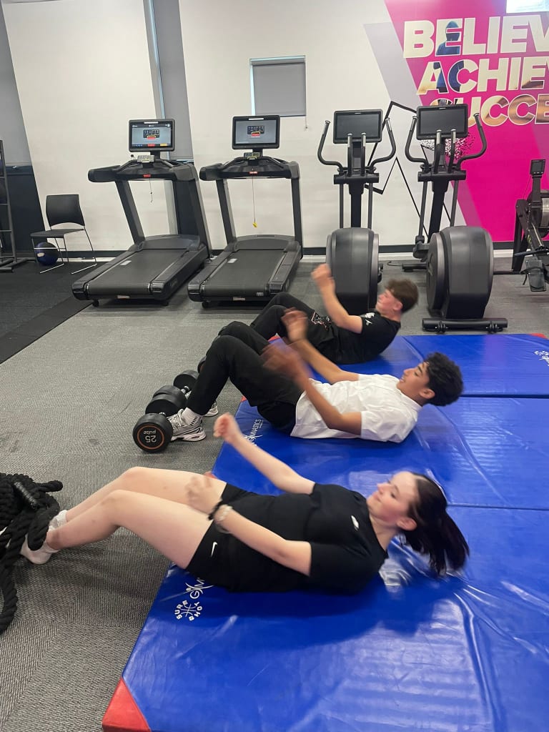 Students training together in the gym beneath a Believe Achieve Succeed wall display